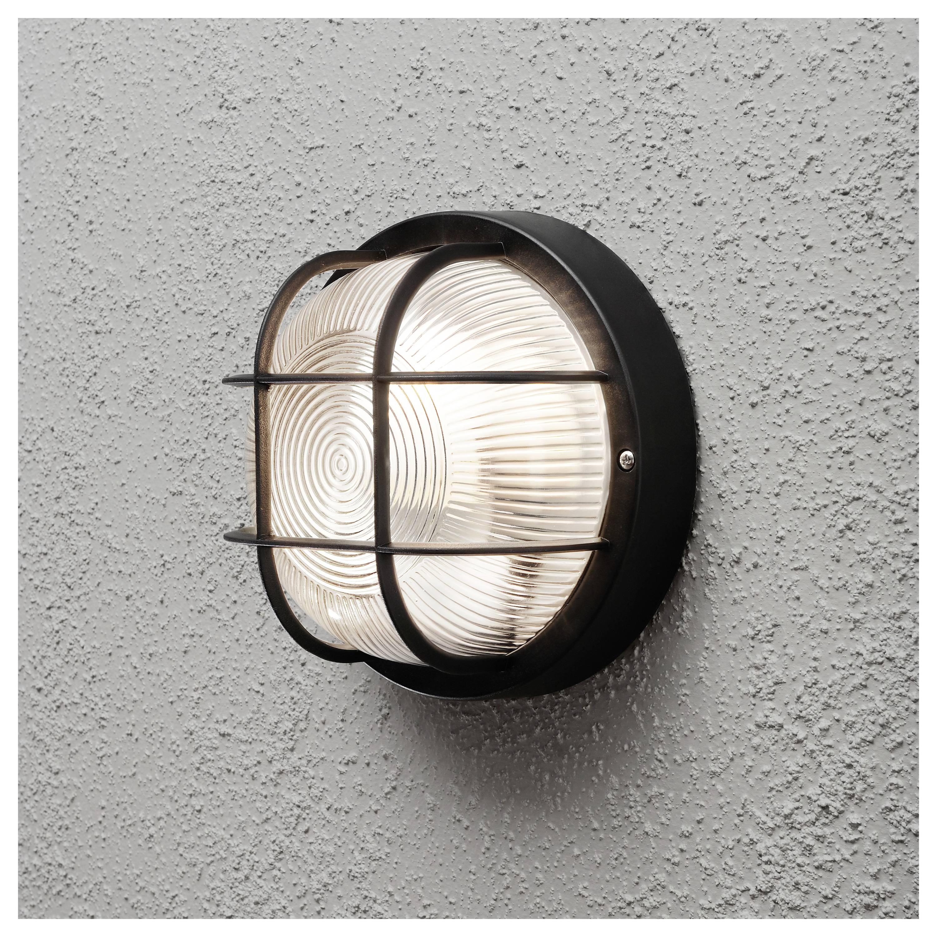 Eine runde Wandleuchte im Industriestil mit Käfigdesign strahlt helles Licht vor einer strukturierten grauen Wand.
