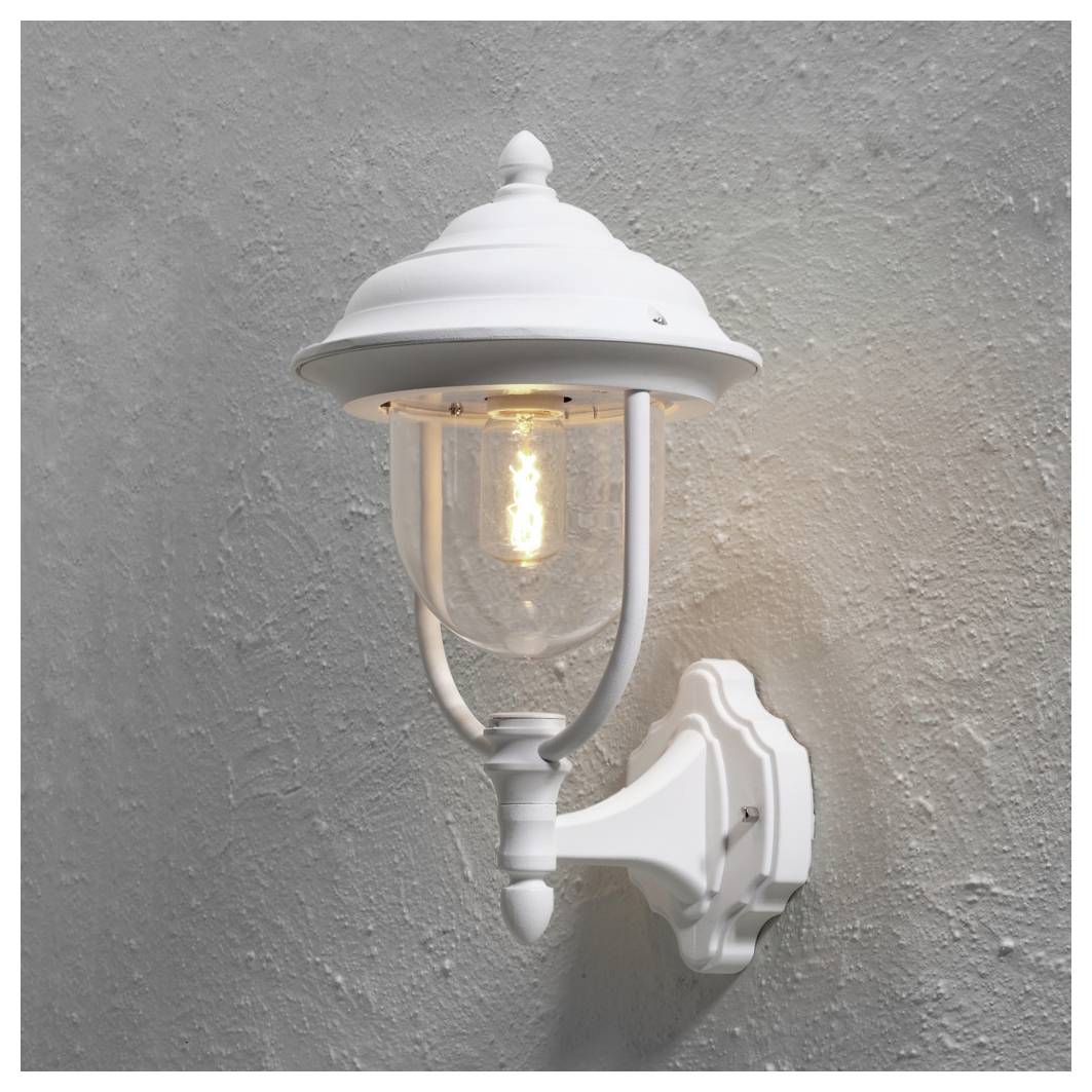 Eine weiße Außenwandlaterne mit traditionellem Design, montiert an einer strukturierten grauen Wand, die ein warmes Licht ausstrahlt.