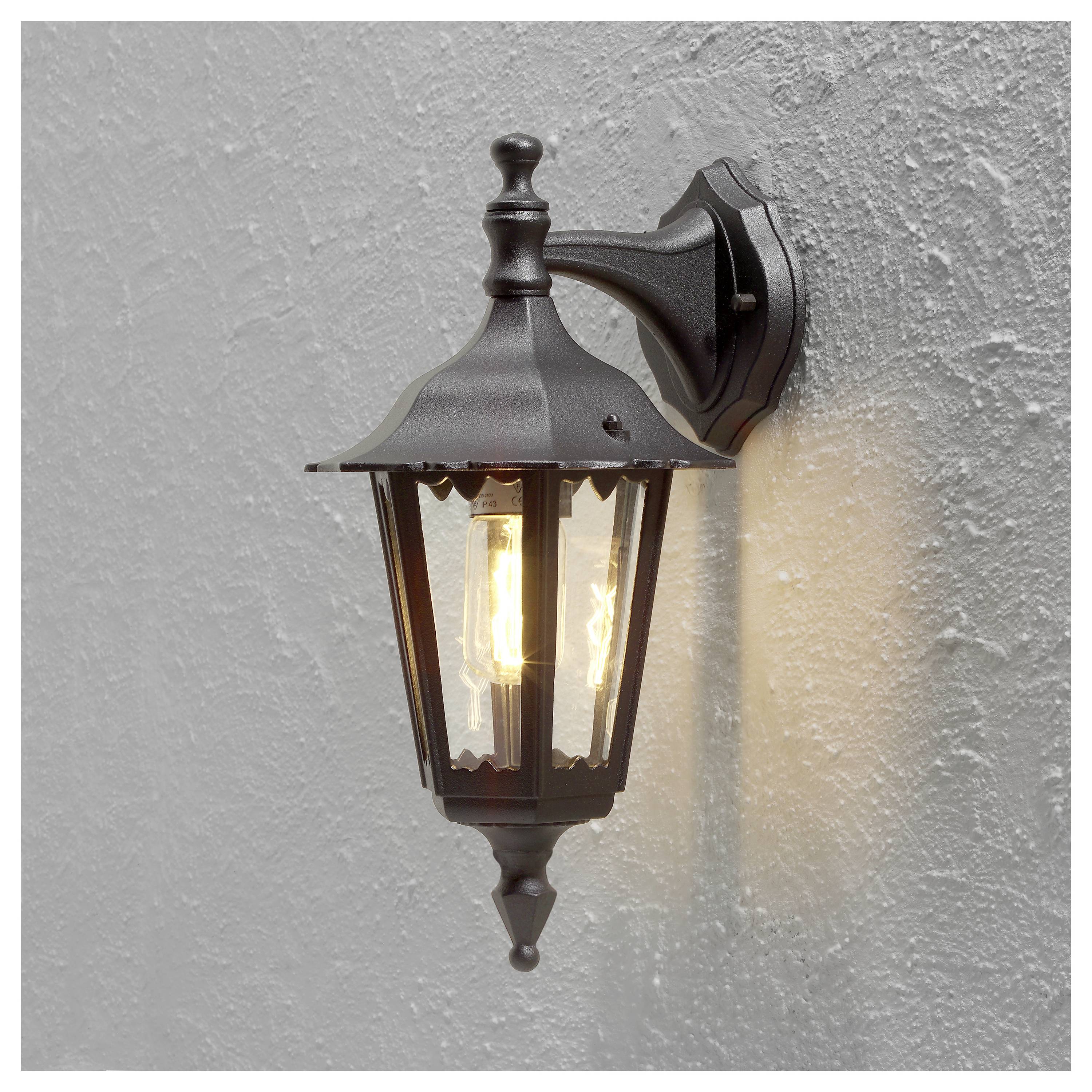 Eine schwarze, traditionelle Wandlaterne im klassischen Stil mit Glasgehäuse, die warmes Licht ausstrahlt, ist an einer strukturierten grauen Wand befestigt.