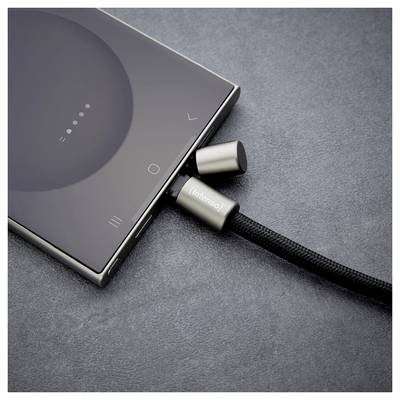 Ein Smartphone wird über ein geflochtenes Kabel mit metallischen Anschlüssen aufgeladen und liegt auf einer dunkelgrauen Oberfläche.