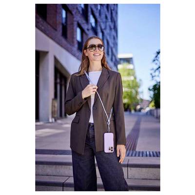 Eine Frau steht im Freien und lächelt, trägt eine Sonnenbrille und eine Jacke, hält ein Telefon mit einem Riemen um den Hals.