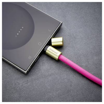 Ein Smartphone, das an ein rosa geflochtenes Ladekabel mit goldenen Anschlüssen, die mit ‚Intenso' beschriftet sind, auf einer grauen Oberfläche angeschlossen ist.