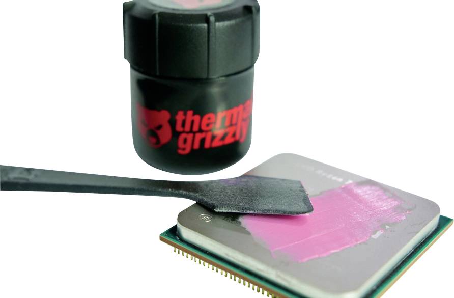 „Ein kleiner schwarzer Behälter mit der Aufschrift „Thermal Grizzly" neben einem Werkzeug, das pinke Wärmeleitpaste auf der Oberfläche eines Computerprozessors verteilt."