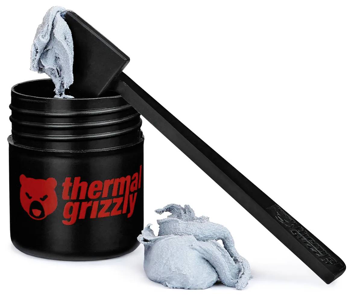Ein schwarzer Behälter mit der Aufschrift "Thermal Grizzly" mit grauer Wärmeleitpaste, die teilweise mit einem schwarzen Spatel ausgehoben wurde, der daneben liegt.