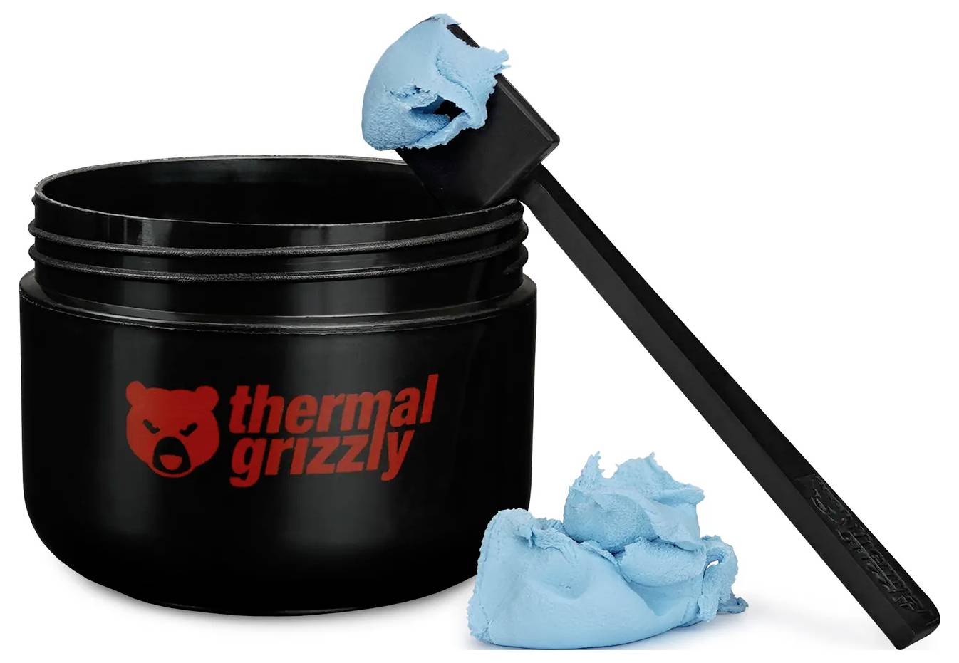 Schwarzer Behälter mit rotem 'Thermal Grizzly' Logo, blaue Wärmeleitpaste auf einem schwarzen Spatel, zusätzliche blaue Paste neben dem Glas.