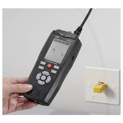Hand hält ein digitales Kabelnetzwerk-Testgerät, das mit einer Wandsteckdose verbunden ist, zeigt ein numerisches Ergebnis auf dem Bildschirm an und deutet auf Testaktivität hin.