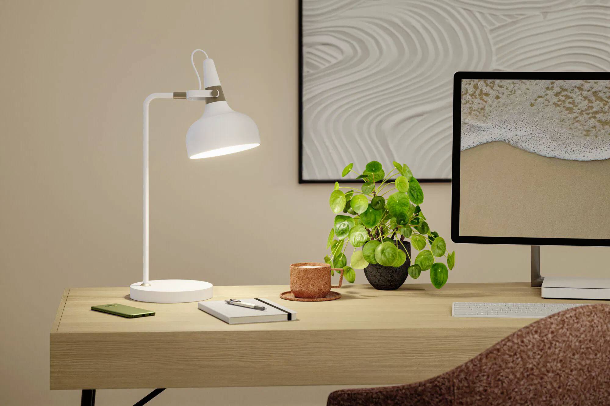 Ein modernes Schreibtisch-Setup mit einer angeschalteten weißen Lampe, einem Computer, der ein Strand-Bild zeigt, einer grünen Pflanze und Büromaterialien auf einer Holzoberfläche.