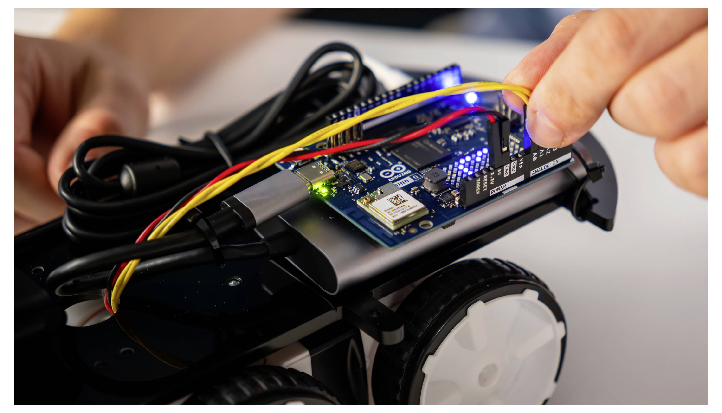 Eine Hand verbindet Kabel mit der Leiterplatte eines kleinen Roboterfahrzeugs und unterstreicht dabei einen Montage- oder Debuggingvorgang.