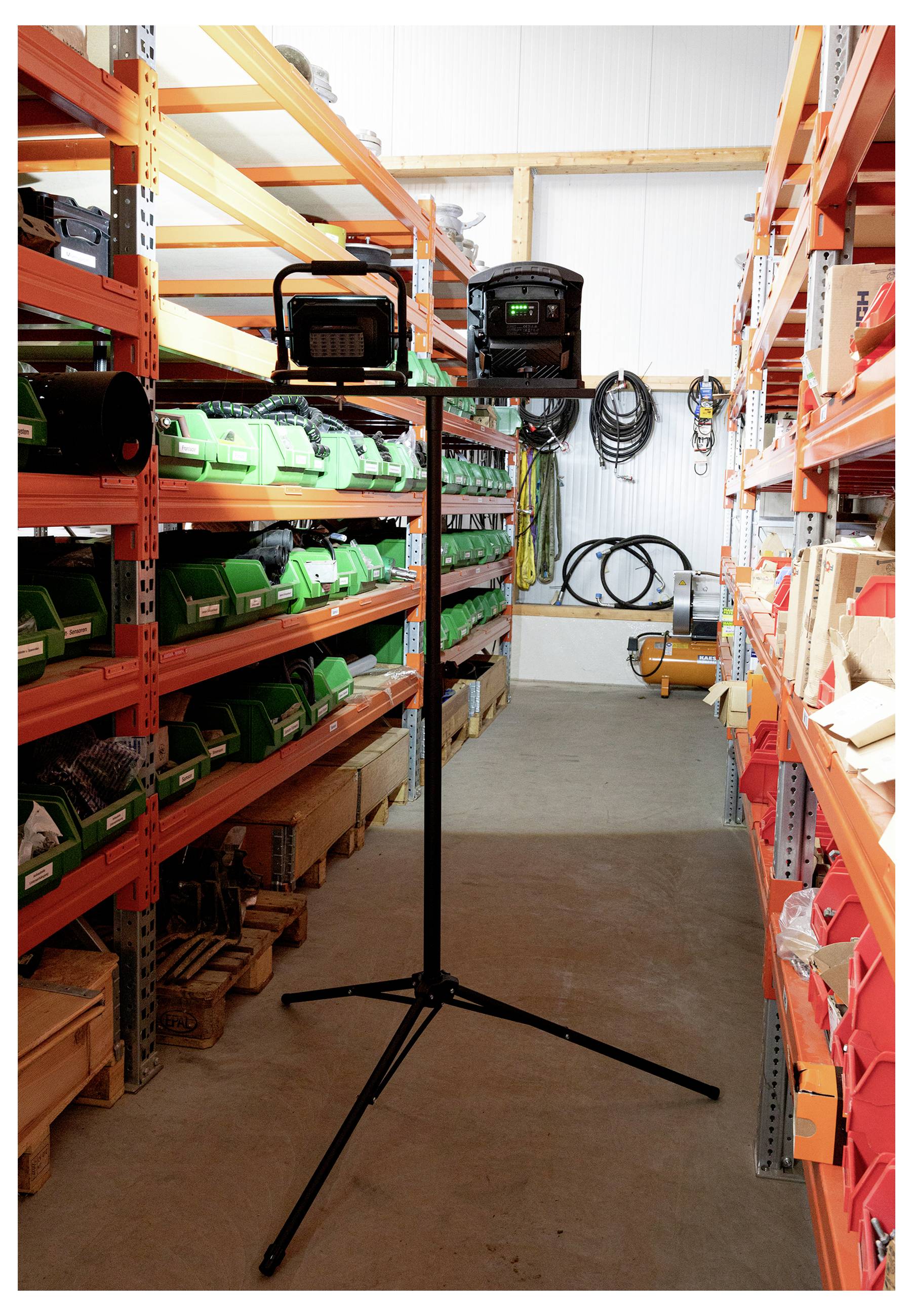 Ein Arbeitsstellenleuchte steht in der Mitte eines Ganges in einem Lagerhaus, umgeben von Regalen, die mit Kartons und grünen Behältern gefüllt sind.