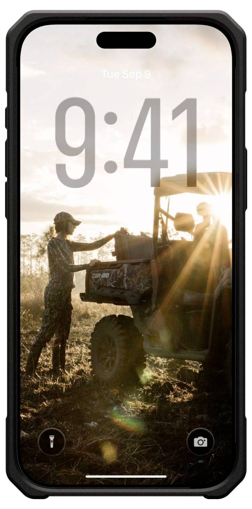 Eine Person in Outdoorausrüstung steht neben einem ATV bei Sonnenuntergang und justiert Ausrüstung am Fahrzeug, während die Sonne durch die Szene scheint.