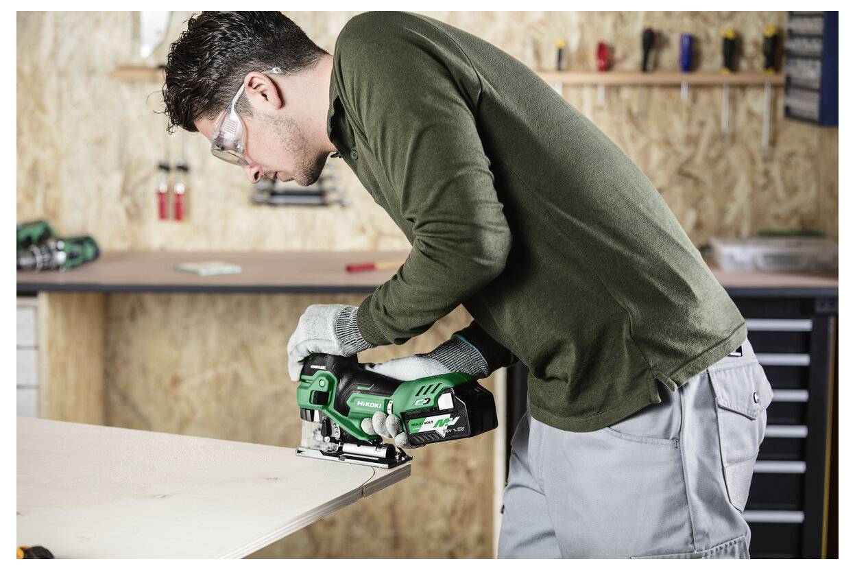 Eine Person mit Schutzbrille benutzt eine Kreissäge, um ein Holzbrett in einer Werkstatt zu sägen und konzentriert sich dabei intensiv auf ihre Aufgabe.