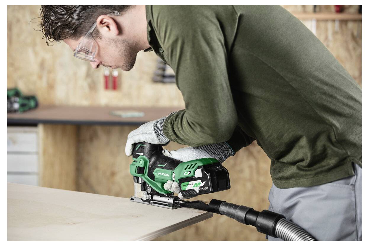 Eine Person mit Sicherheitsausrüstung verwendet eine Stichsäge, um ein Holzstück in einer Werkstattumgebung zu schneiden.