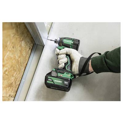 Eine Person mit Handschuhen benutzt einen grünen Akkuschrauber, um einen Metallrahmen auf einem Betonboden neben einer Holzwand zu befestigen.