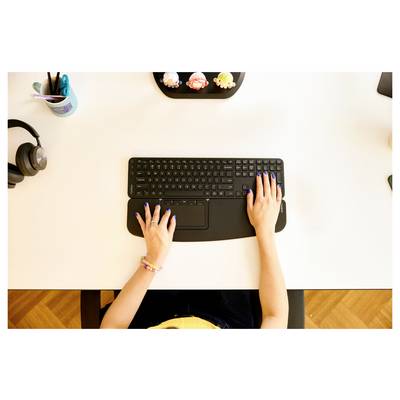 Eine Person, die auf einer Tastatur an einem Schreibtisch tippt, umgeben von verschiedenen Büromaterialien.
