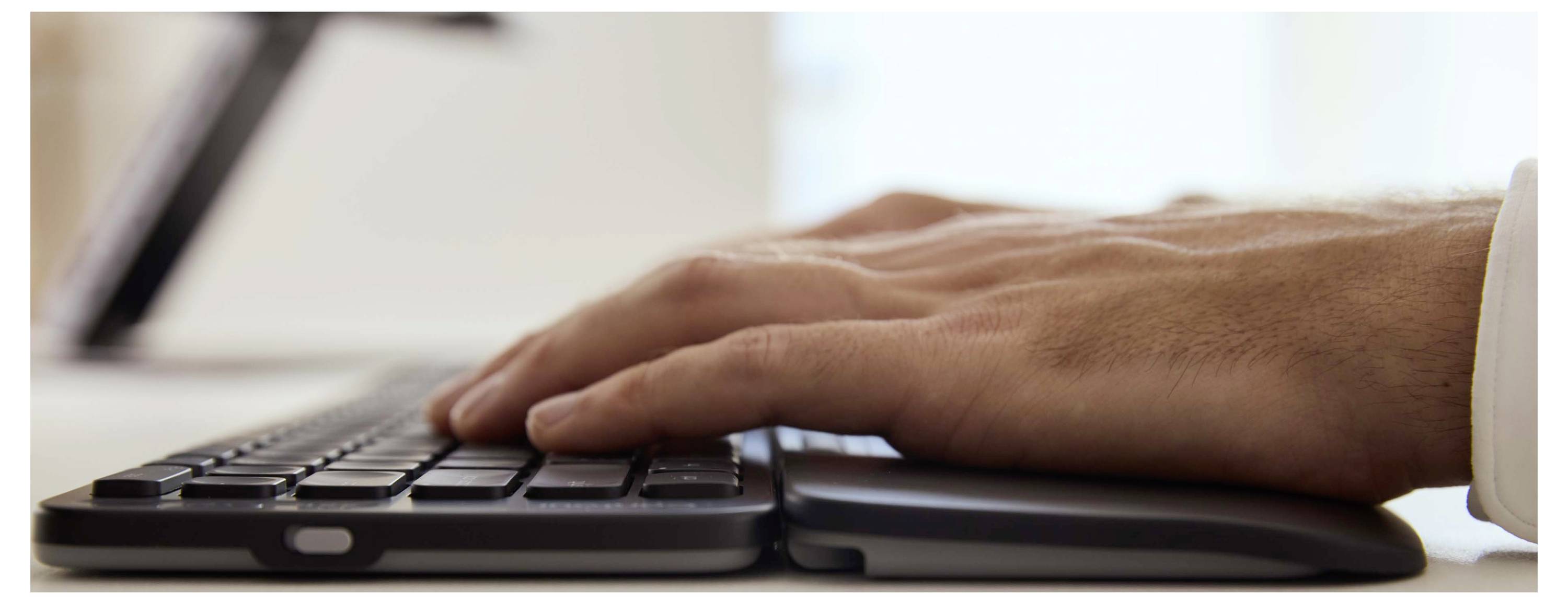 Eine Nahaufnahme von Händen, die auf einer Tastatur tippen und Arbeit oder Kommunikation in einem technologieorientierten Umfeld andeuten.