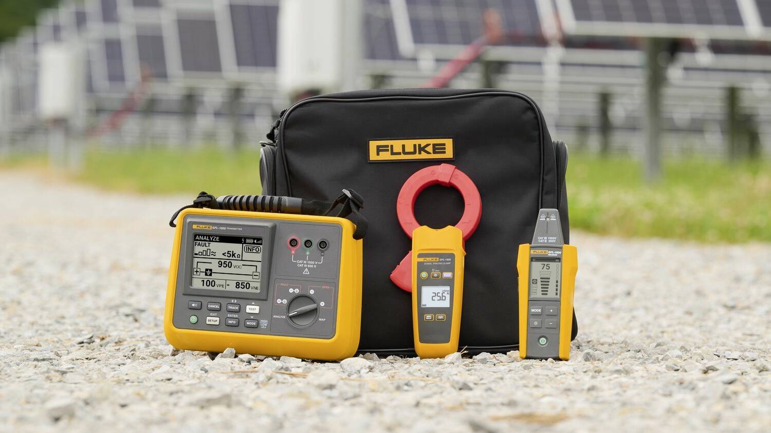 Elektrische Prüfgeräte der Marke 'Fluke', einschließlich Multimeter und Zangenmessgerät, auf Kies mit Solarpanels im Hintergrund.