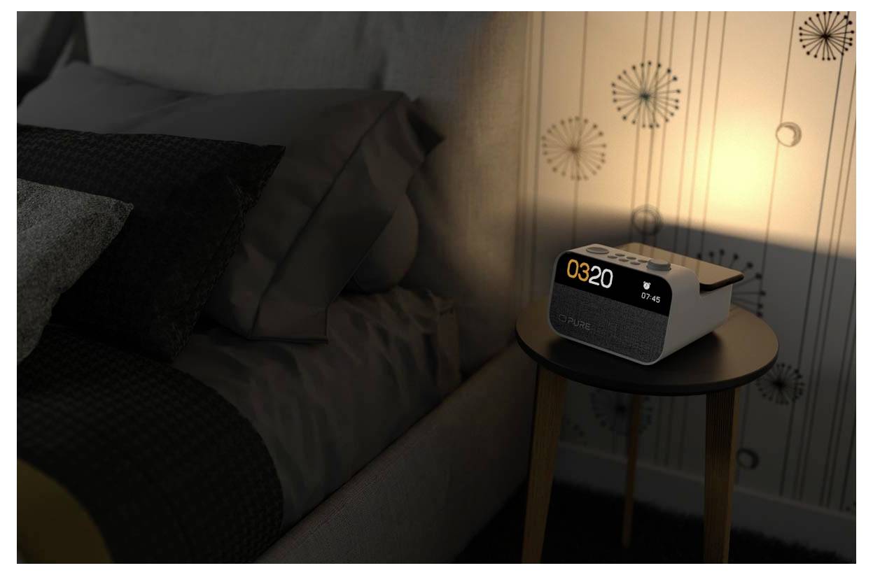 Eine digitale Alarmuhr mit der Anzeige '03:20' steht auf einem Nachttisch neben einem Bett und wird von einem weichen, warmen Licht in einem dunklen Raum beleuchtet.