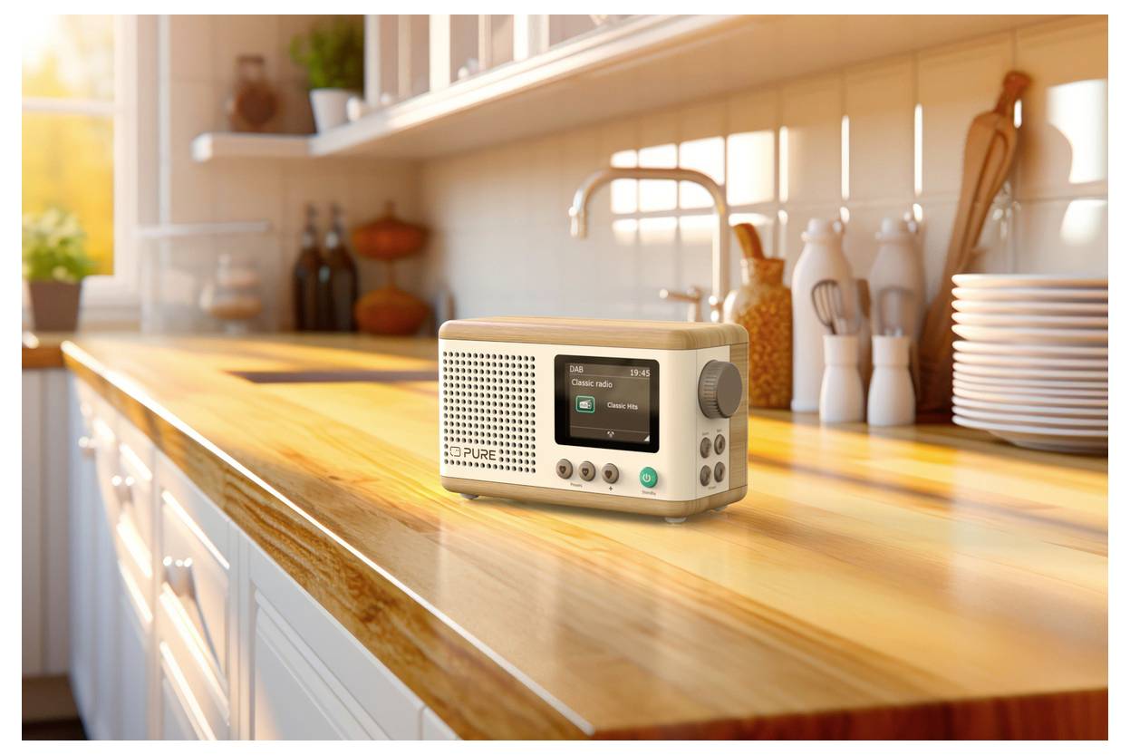 Ein kleines digitales Radio steht auf einem sonnenbeschienenen Holzküchenzähler. Die Küche hat weiße Schränke und verschiedene Küchenutensilien im Hintergrund.