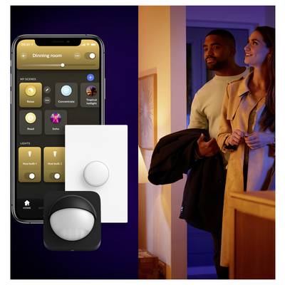 Ein Smartphone zeigt eine Hausbeleuchtungs-App mit verschiedenen Lichteinstellungen. Ein Paar betritt einen warm beleuchteten Raum und deutet damit auf eine intelligente Hausbeleuchtungssteuerung hin.