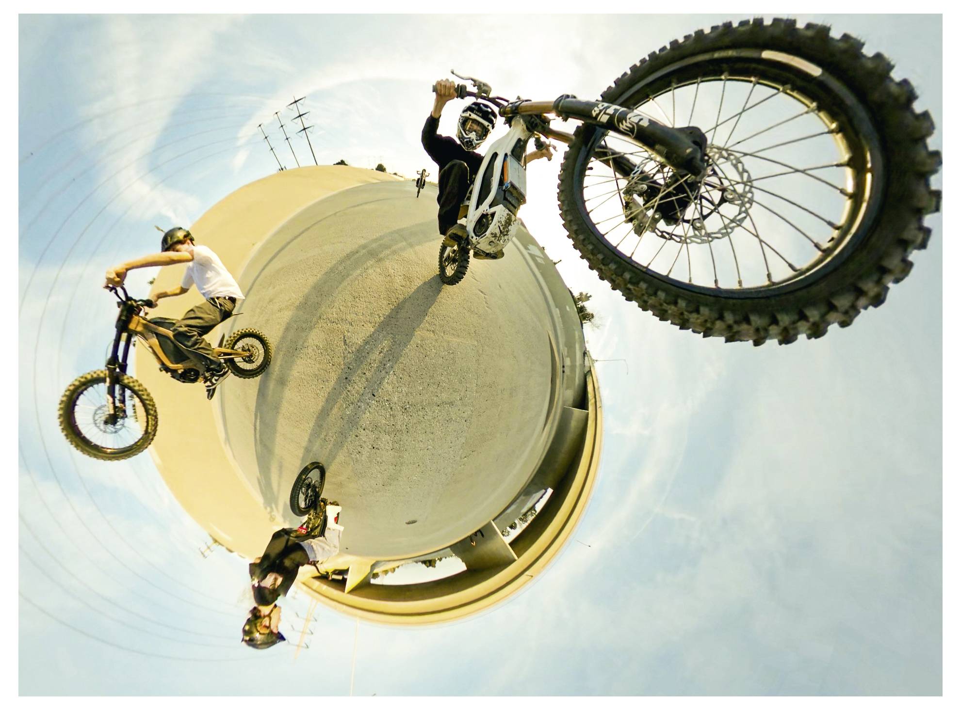 Motorradfahrer, die auf einer Kurve unter einem blauen Himmel Stunts vorführen und dabei dynamische Bewegung und Balance demonstrieren.