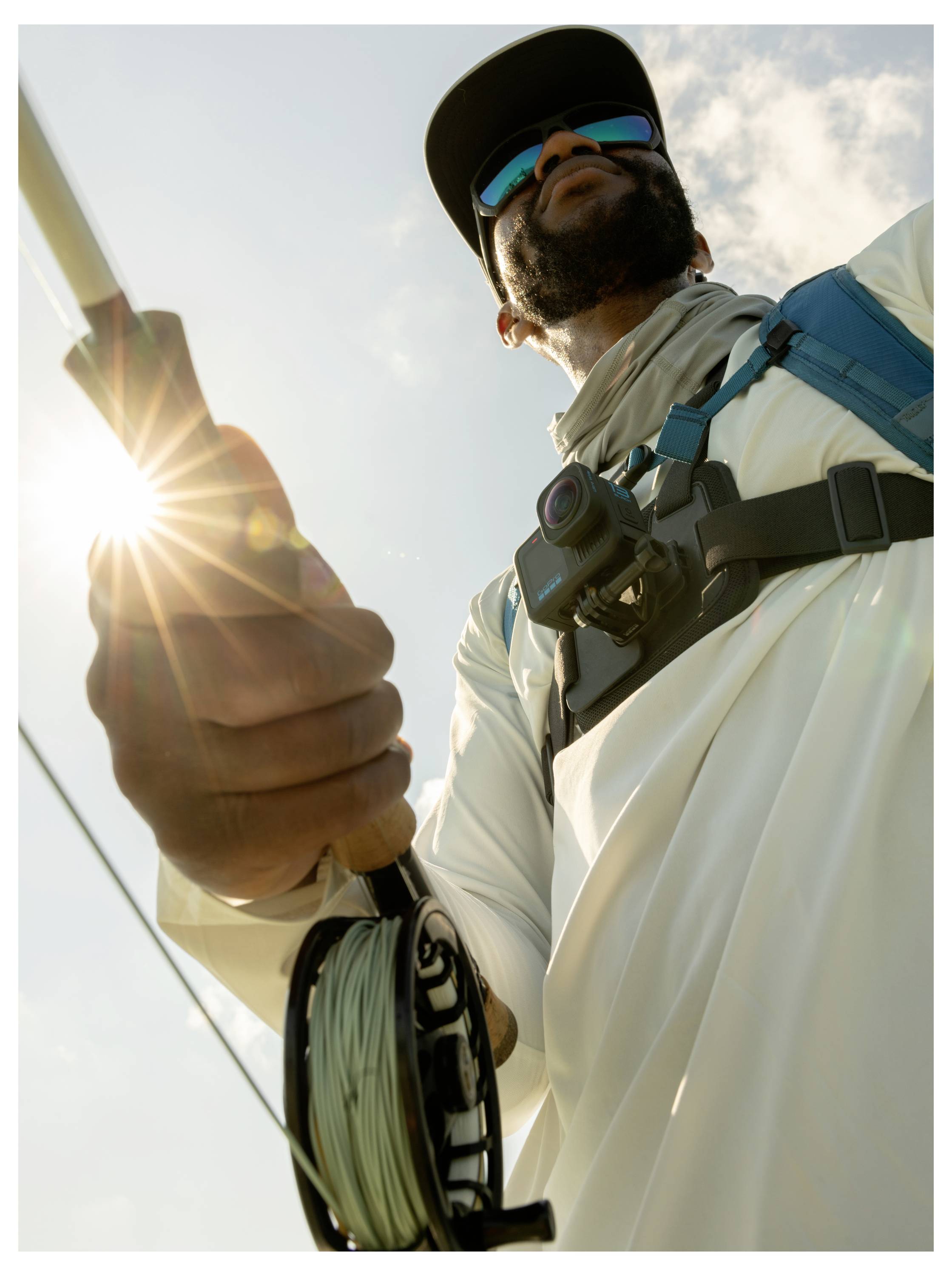 Eine Person mit Hut und Sonnenbrille, die eine Angelrute unter einem strahlend hellen Himmel hält. Der Blickwinkel betont die Sonnenstrahlen und die Angelausrüstung.