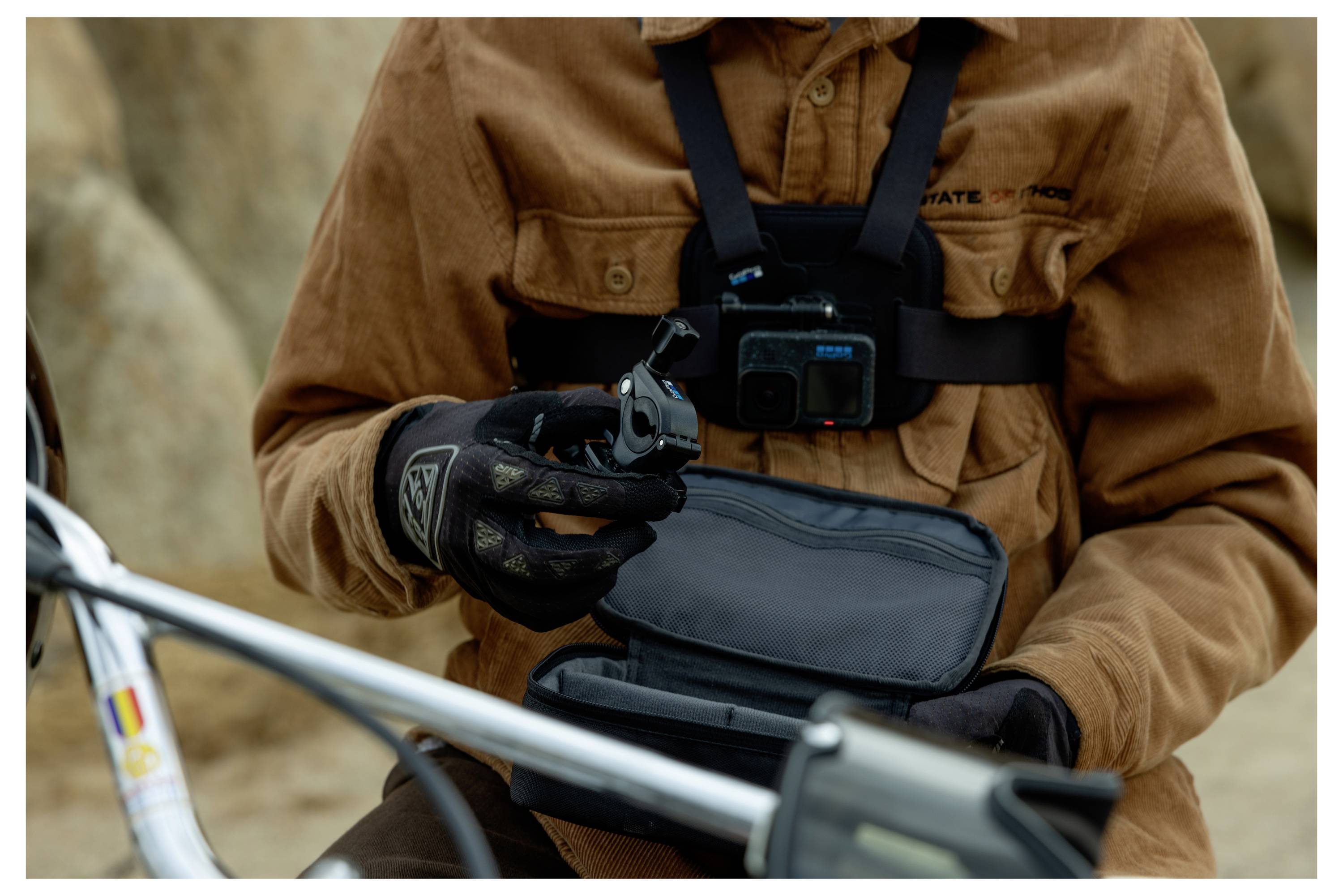 Eine Person mit einer am Körper getragenen Kamera hält ein kompaktes Kameragerät neben einem Fahrrad, was auf Aktivitäten zur Außenaufnahme hindeutet.