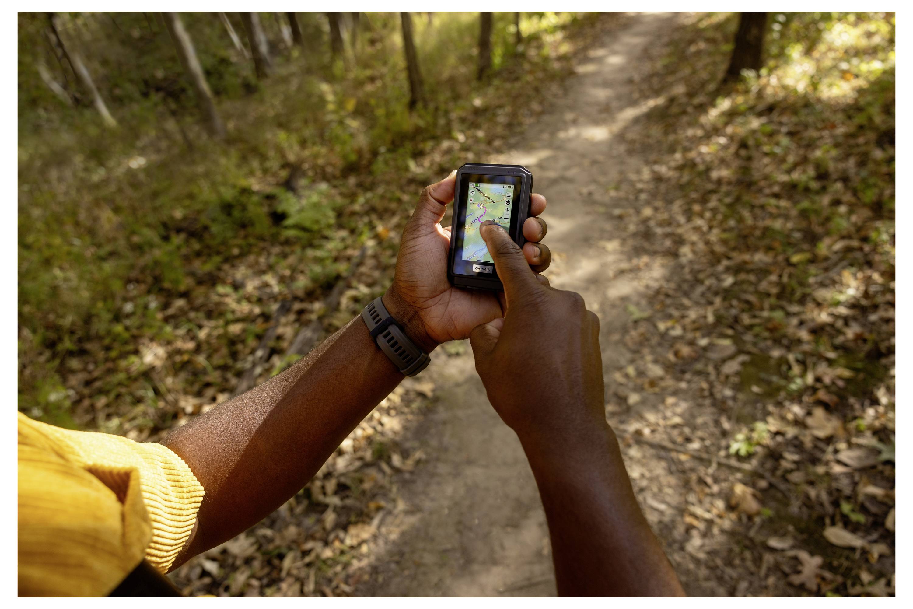 Eine Person nutzt ein GPS-Gerät, um einen Waldweg zu navigieren, umgeben von Bäumen und Herbstlaub.