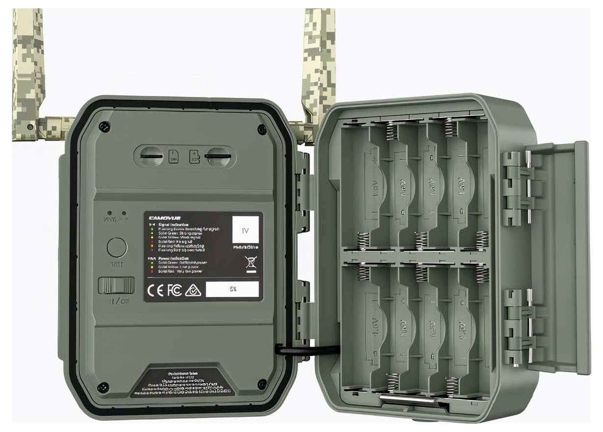 Grüne Wildkamera geöffnet, um das Batteriefach mit Platz für mehrere Batterien zu zeigen. Tarnfarbene Riemen sind oben sichtbar.