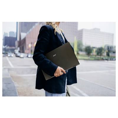 Eine Person mit einem Laptop steht an einer städtischen Kreuzung, im Hintergrund sind Stadtgebäude zu sehen, was einen Geschäfts- oder Reisekontext andeutet.