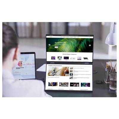 Eine Person arbeitet an einem Schreibtisch mit einem Laptop mit Doppelbildschirm, auf dem eine Tech-Website-Startseite angezeigt wird. Ein zweiter Bildschirm zeigt ein buntes Diagramm mit Daten.