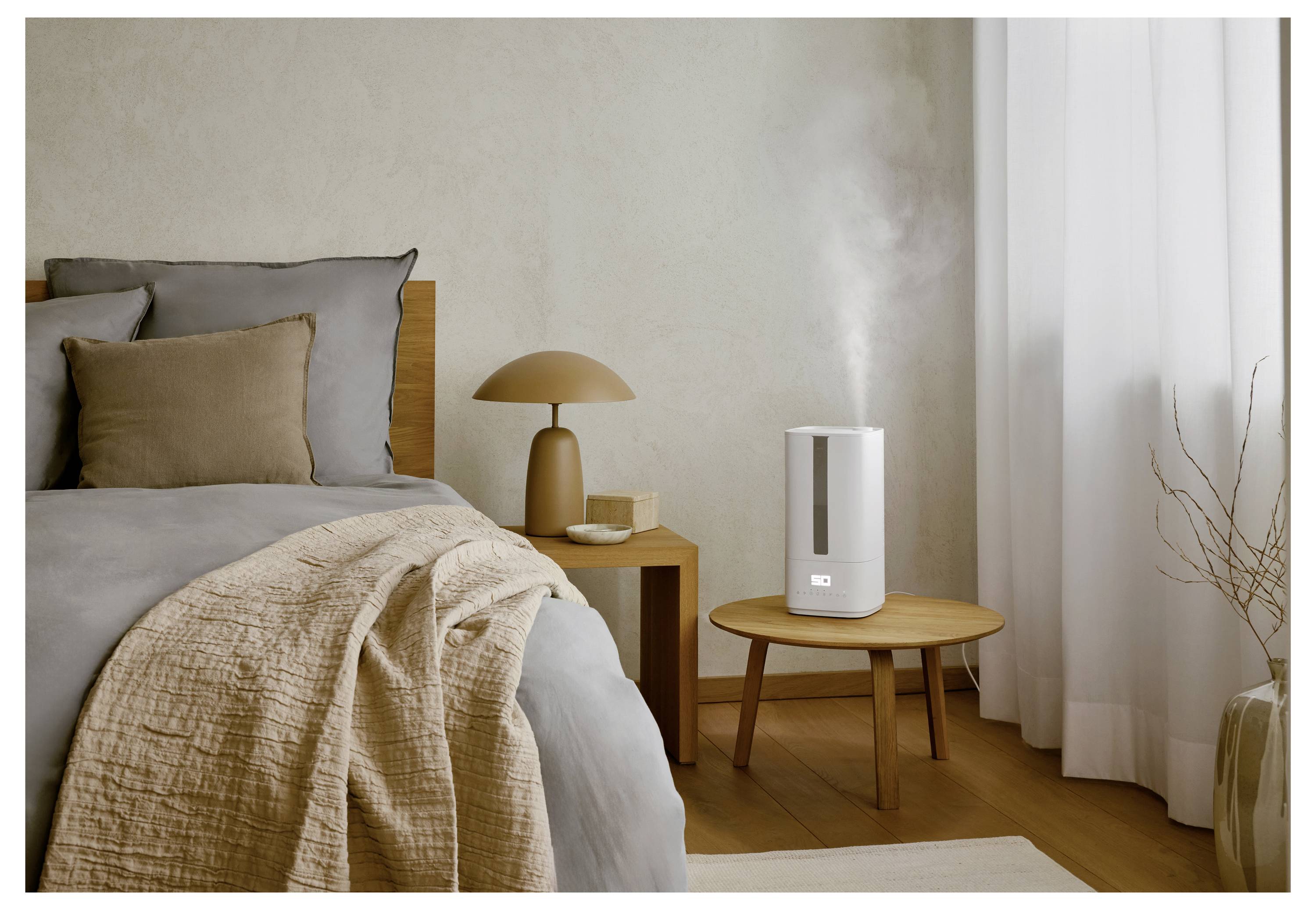 Ein gemütliches Schlafzimmer in neutralen Farbtönen zeigt ein ordentlich gemachtes Bett und einen Holznachttisch, auf dem ein moderner Luftbefeuchter Nebel verströmt.