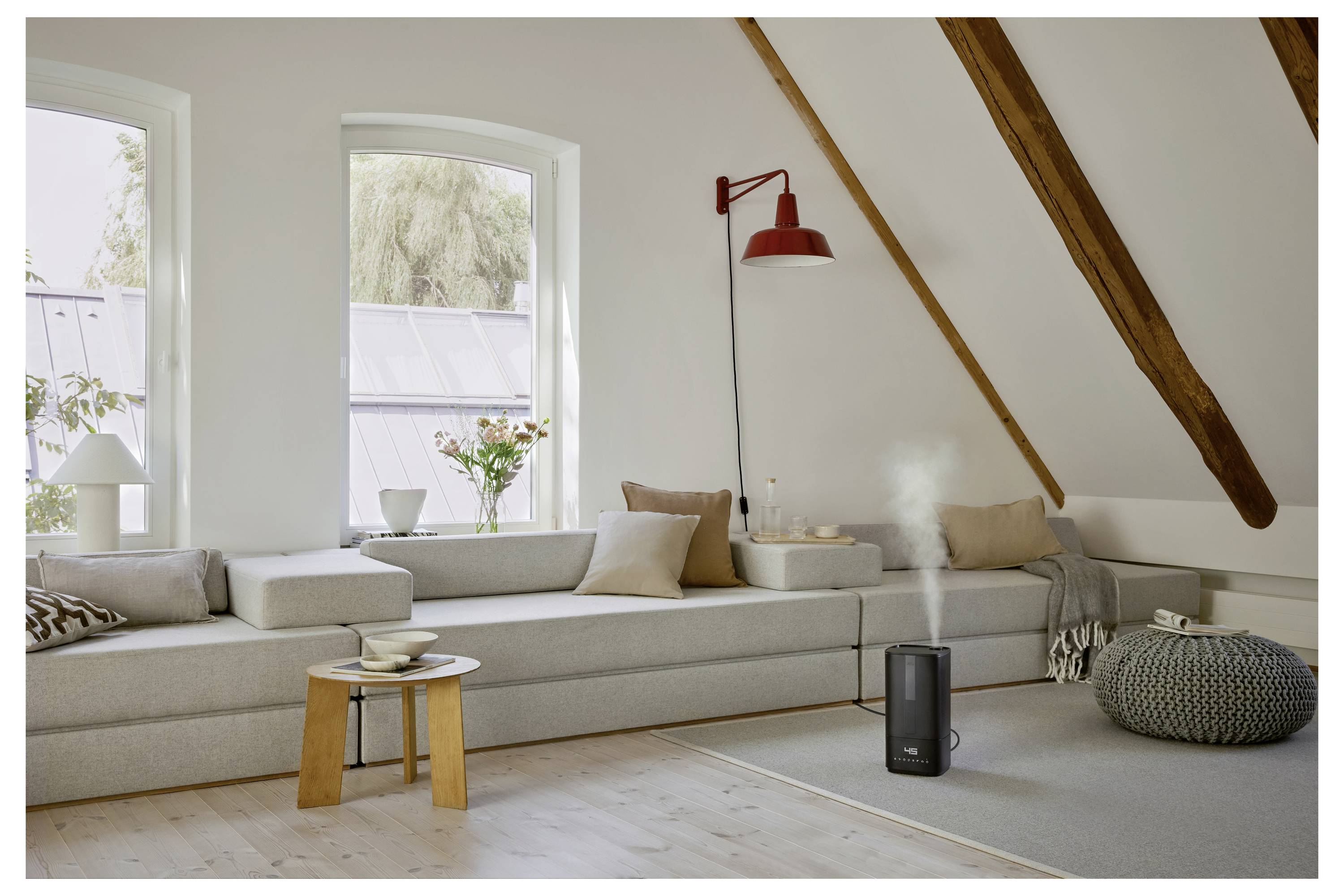 Geräumiges Wohnzimmer mit minimalistischem Design, ausgestattet mit einem hellgrauen Ecksofa, einer roten Wandlampe und einem schwarzen Luftbefeuchter, der Dampf abgibt.