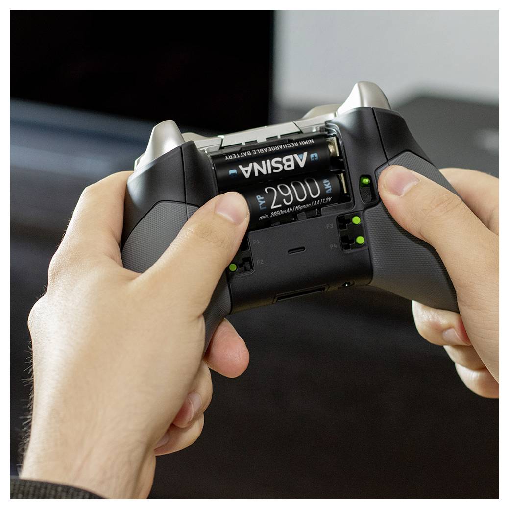 Hände, die einen Gamecontroller von hinten halten, wobei das Batteriefach geöffnet ist und 'ADSIMA' AA-Batterien im Inneren sichtbar sind.