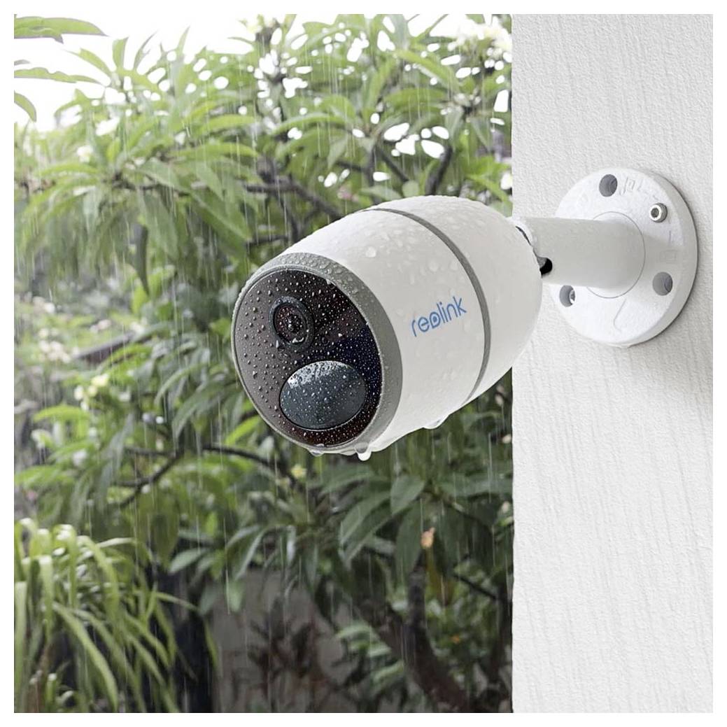 Eine Sicherheitskamera, die an einer Außenwand an einem regnerischen Tag befestigt ist, mit sichtbaren Wassertropfen auf ihrer Oberfläche und Grünpflanzen im Hintergrund.