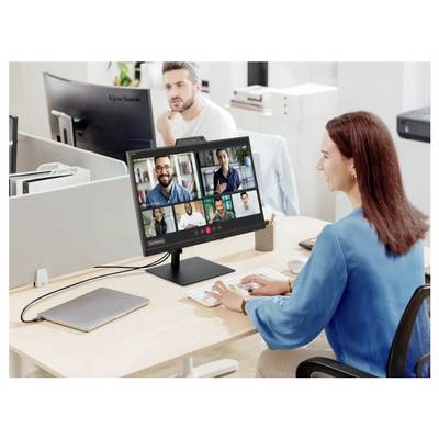 Eine Frau an einem Schreibtisch nimmt an einer Videokonferenz auf ihrem Computerbildschirm teil, auf dem mehrere Teilnehmer zu sehen sind. Ein offener Laptop liegt in der Nähe.