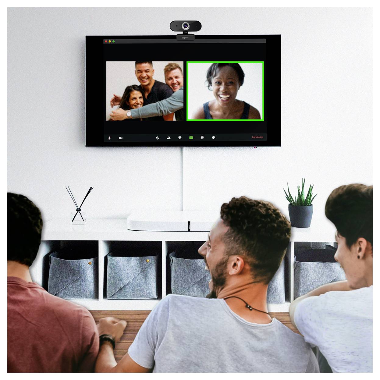 Menschen in einem Raum bei einer Videokonferenz mit vier Personen auf dem Bildschirm, die eine virtuelle Besprechungssituation veranschaulicht.