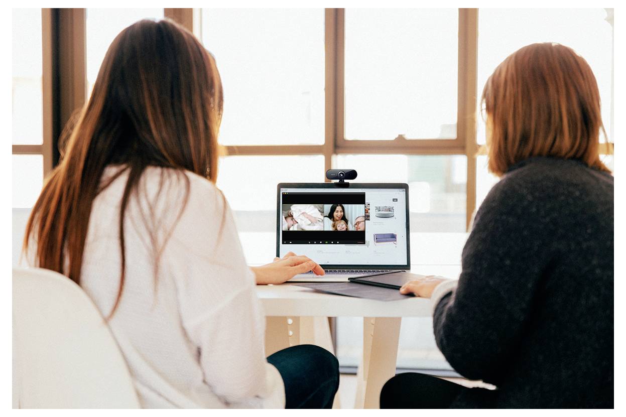 Zwei Personen sitzen an einem Tisch und diskutieren über Videoinhalte, die auf dem Bildschirm eines Laptops in einem hellen Raum angezeigt werden.