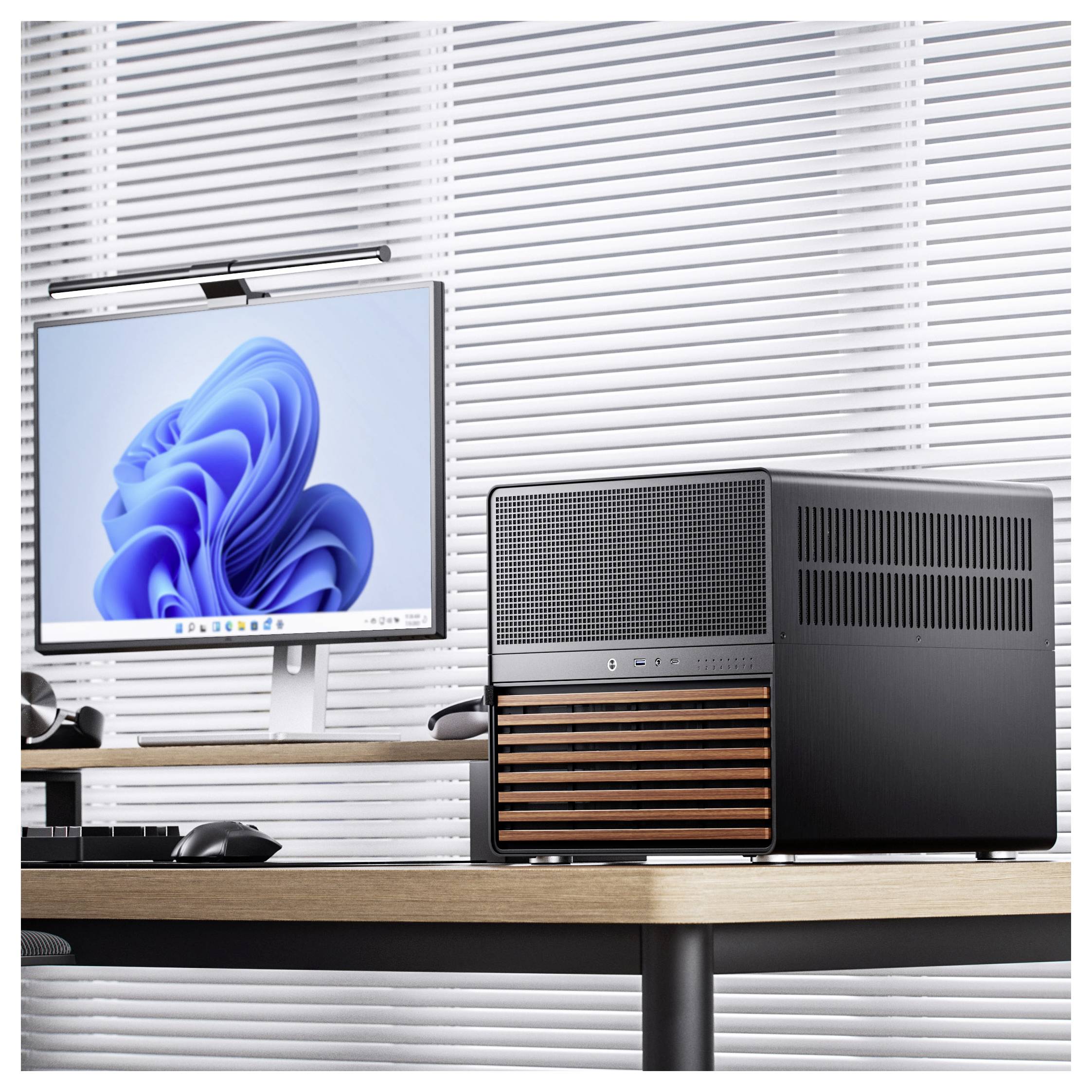 Eine moderne Computereinrichtung auf einem Holzschreibtisch mit einem würfelförmigen schwarzen PC-Gehäuse mit Holzelementen und einem Monitor, der ein blaues abstraktes Muster zeigt.