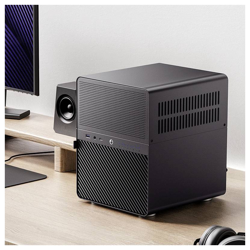 Ein schlanker, schwarzer Desktop-Computer auf einem Holzschreibtisch neben einem Monitor und einem Lautsprecher, was eine moderne Büro- oder Heimarbeitsplatz-Einrichtung andeutet.