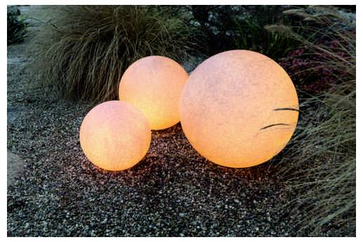 Drei runde, leuchtende Gartenlampen in unterschiedlichen Größen, die auf einem Kiesbett platziert sind und von Ziergräsern umgeben sind, schaffen eine stimmungsvolle Outdoor-Atmosphäre.