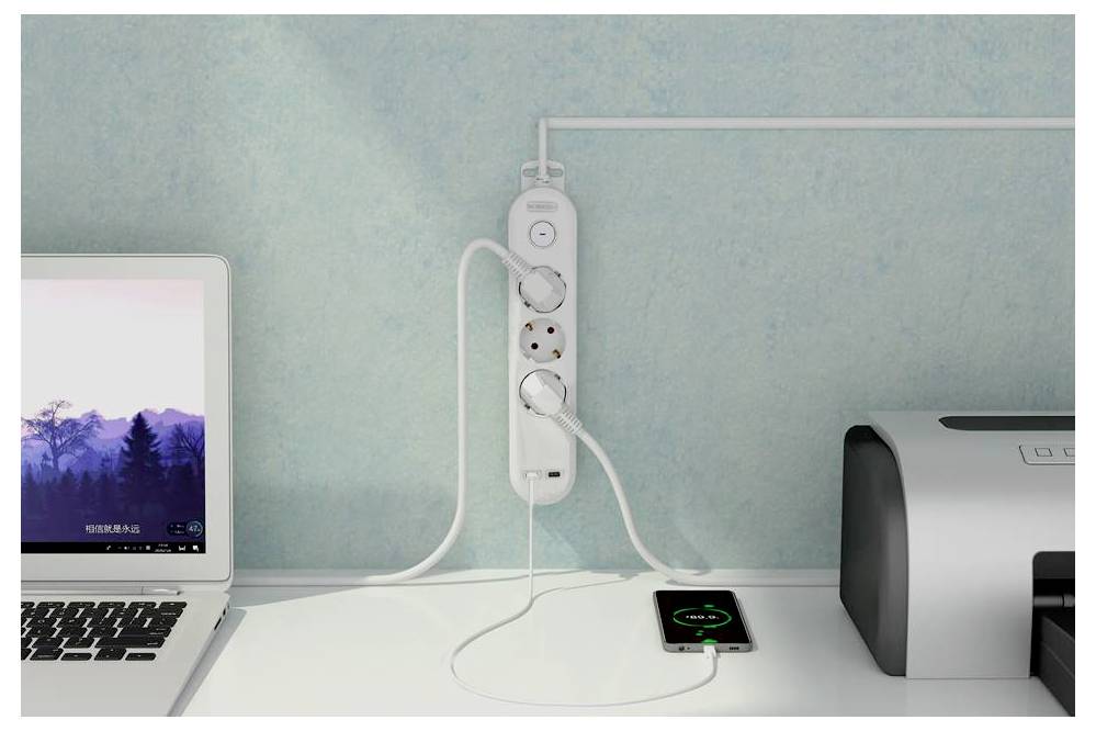Eine Steckdosenleiste, an der Wand montiert, mit einem eingesteckten Telefon und Laptop, die gerade aufgeladen werden; ein Drucker steht in der Nähe auf dem Schreibtisch.