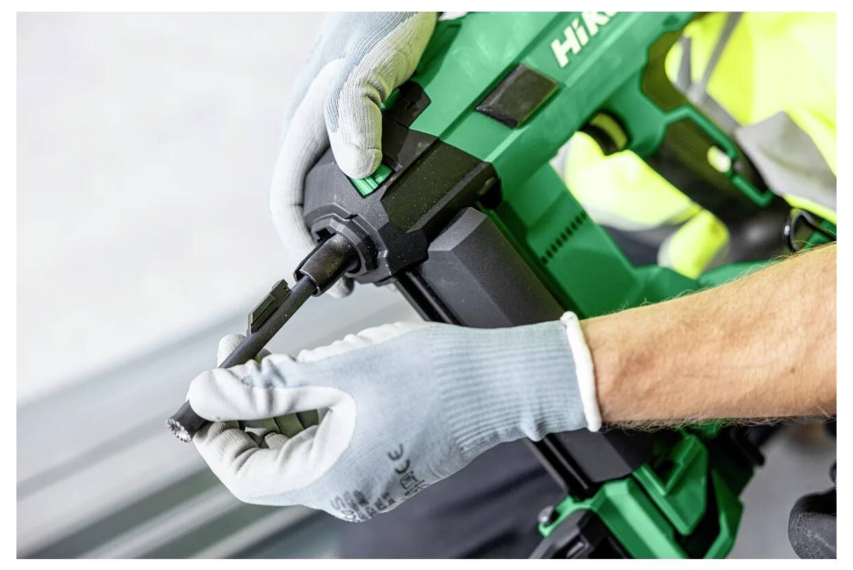 Eine Person mit Handschuhen justiert ein grünes Elektrowerkzeug und konzentriert sich dabei auf den Bohrer, was auf Vorbereitung oder Wartungsarbeiten hindeutet.
