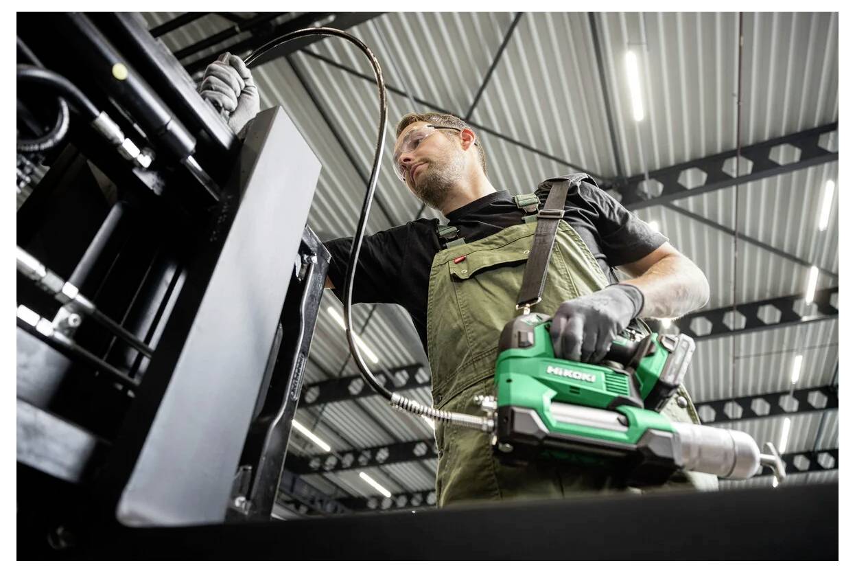 Ein Arbeiter in Schutzausrüstung bedient ein Elektrowerkzeug an einer Maschine in einer großen Industrieanlage und konzentriert sich auf Wartungs- oder Montagearbeiten.