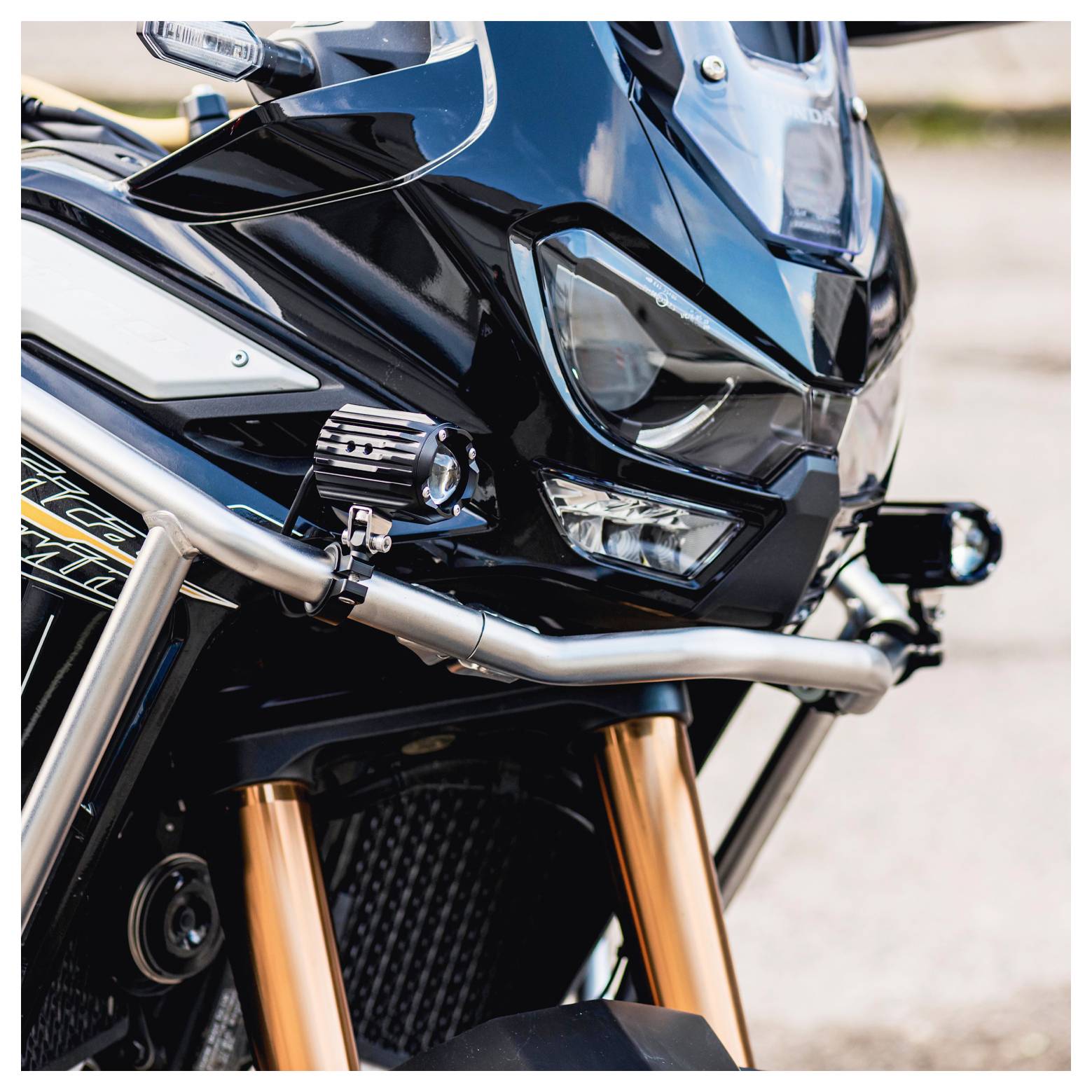 Nahaufnahme der Frontpartie eines Motorrads mit schlanker schwarzer Verkleidung, scharfkantig geformten Scheinwerfern und robusten Metallstreben vor einem klaren blauen Himmel.