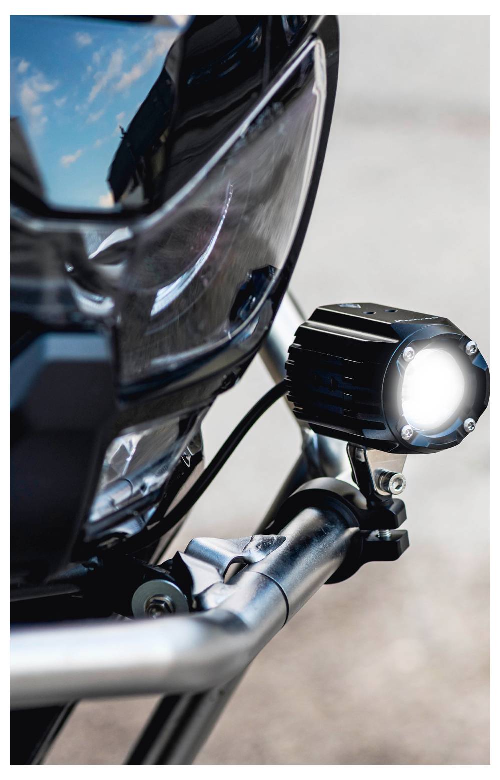 Nahaufnahme der Motorradfront, die einen Scheinwerfer und eine Zusatzbeleuchtung präsentiert und ein schlankes Design sowie eine verchromte Oberfläche hervorhebt.