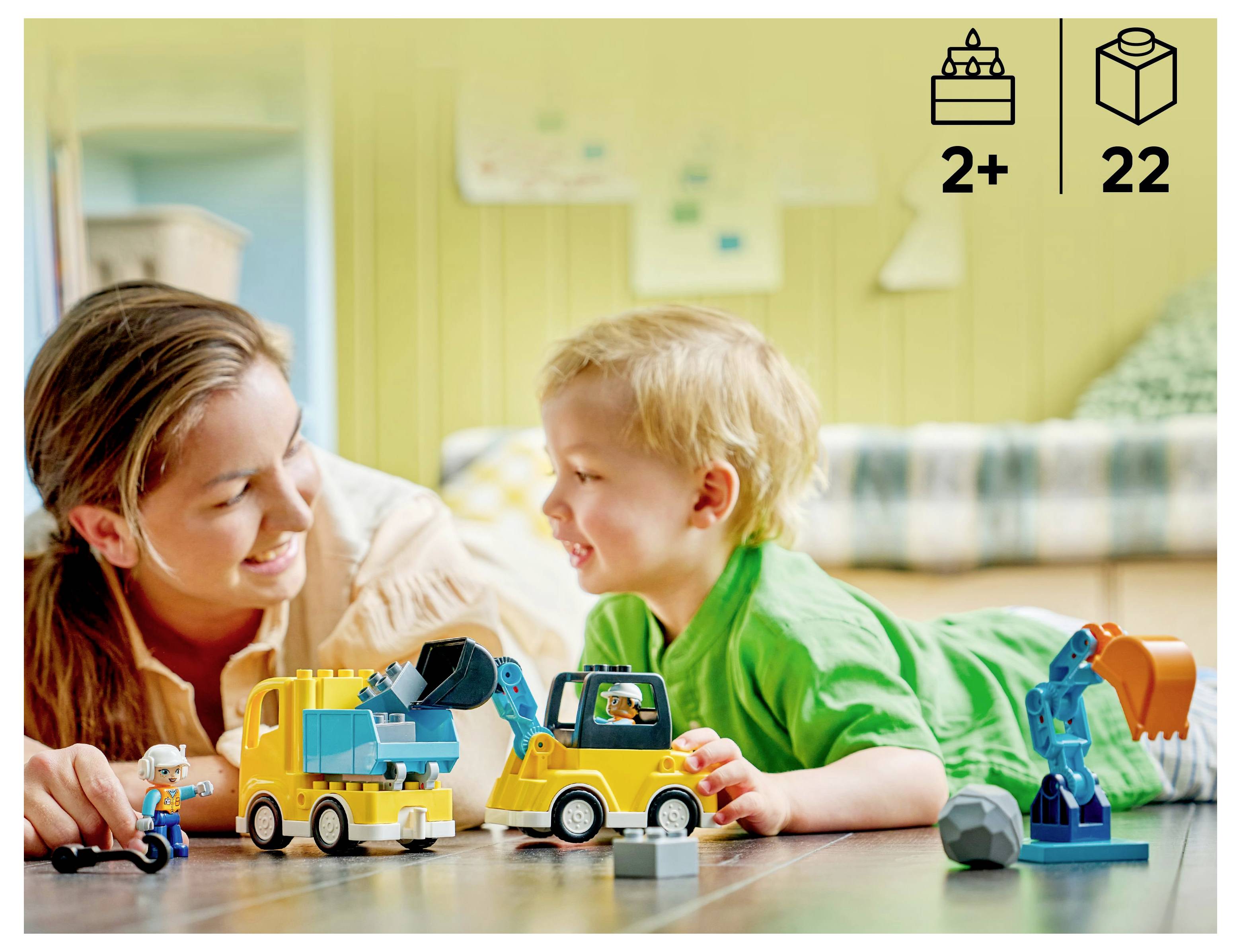 Ein Erwachsener und ein Kind spielen mit Spielzeug-Baufahrzeugen in einem gemütlichen Raum. Die Verpackung zeigt, dass das Spielzeug für Kinder ab 2 Jahren geeignet ist und 22 Teile enthält.