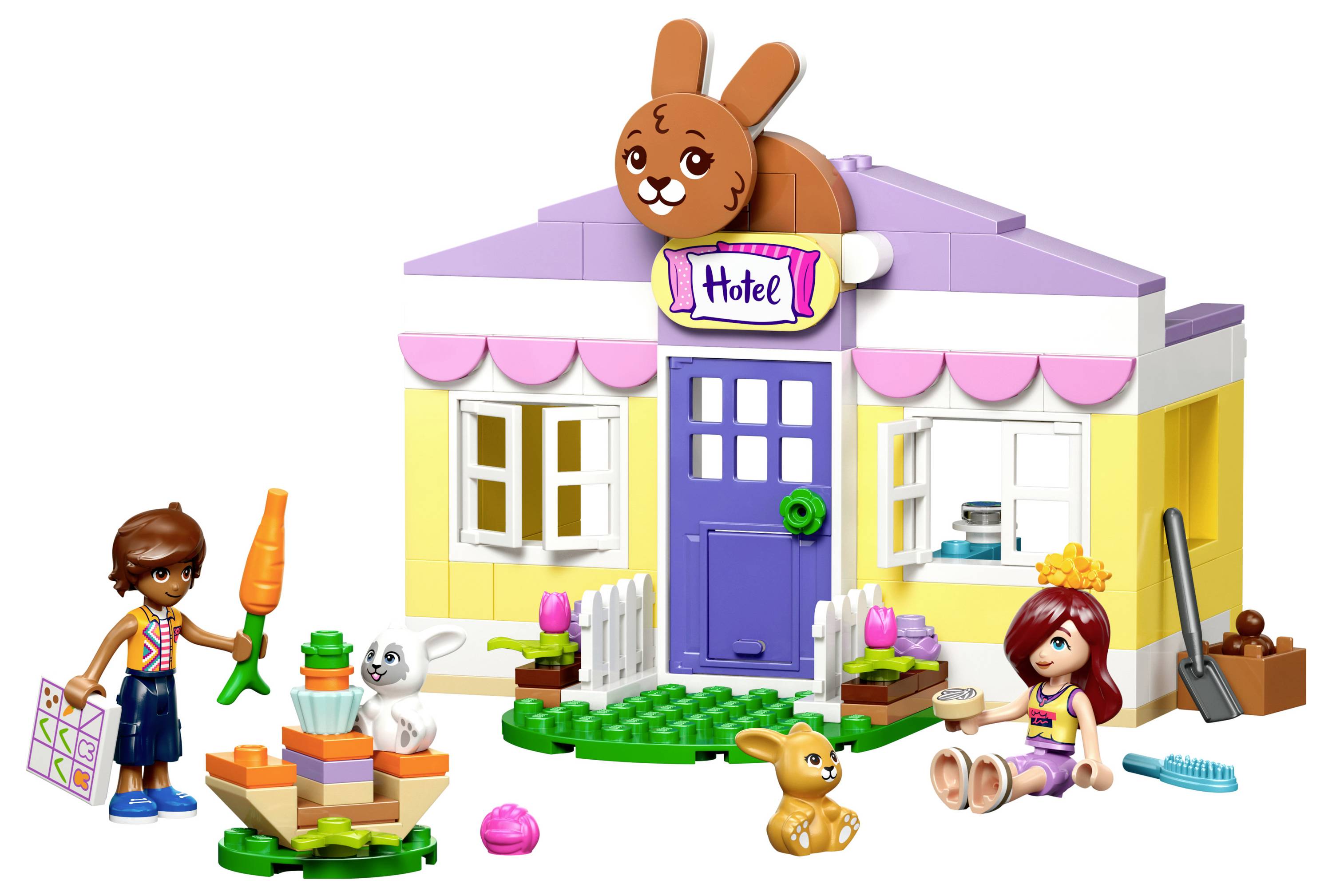 Ein kleines Spielzeuggebäude mit einer lila Tür und einem Schild mit der Aufschrift "Hotel". Kinderfiguren, ein Möhrenschild und Spielzeughasen stehen davor.