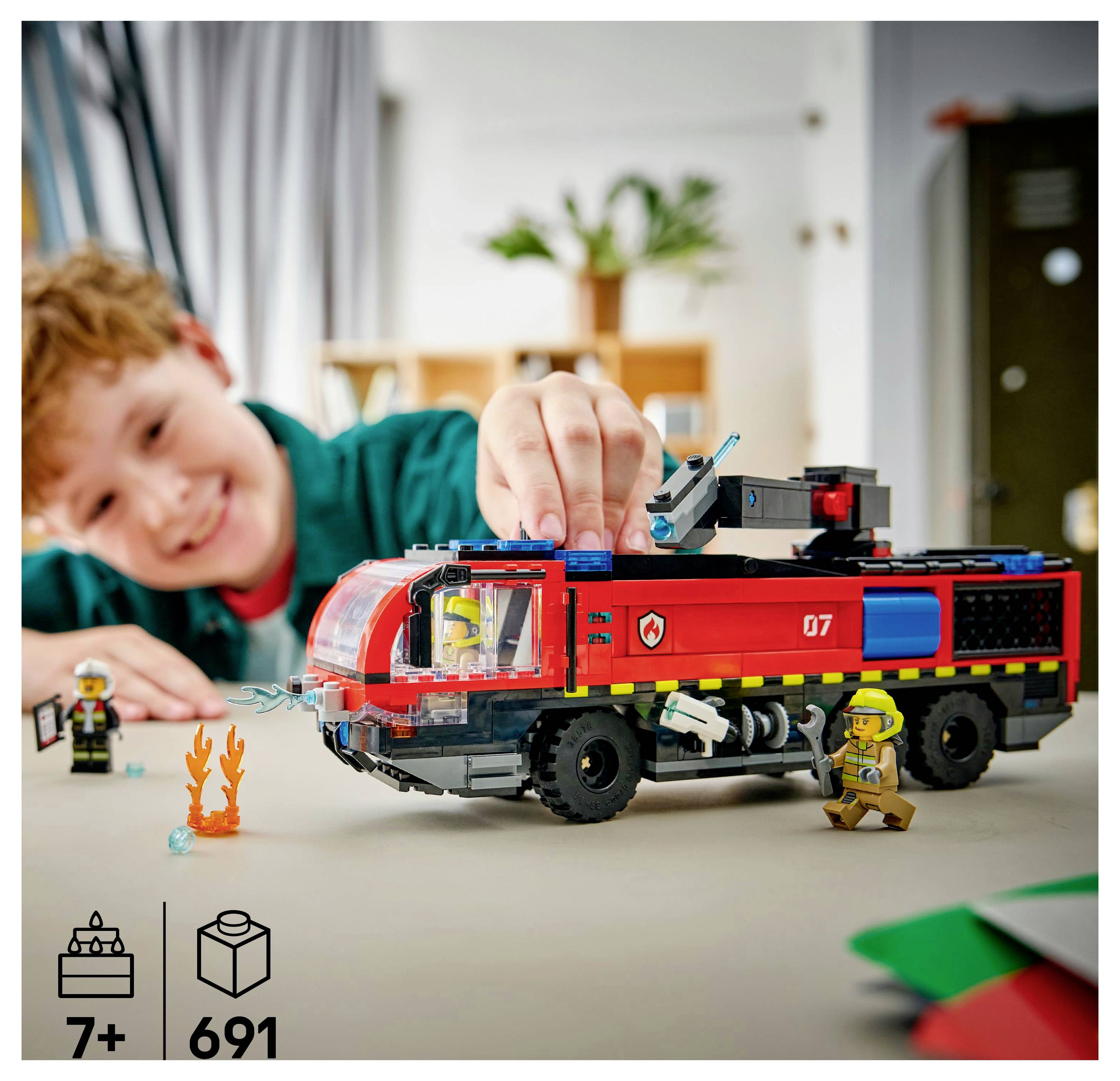Ein Kind, das mit einem Feuerwehr-LEGO-Set spielt, mit Feuerwehrleuten und Flammen. Das Bild zeigt die Altersempfehlung '7+' und die Anzahl der Teile als '691'.