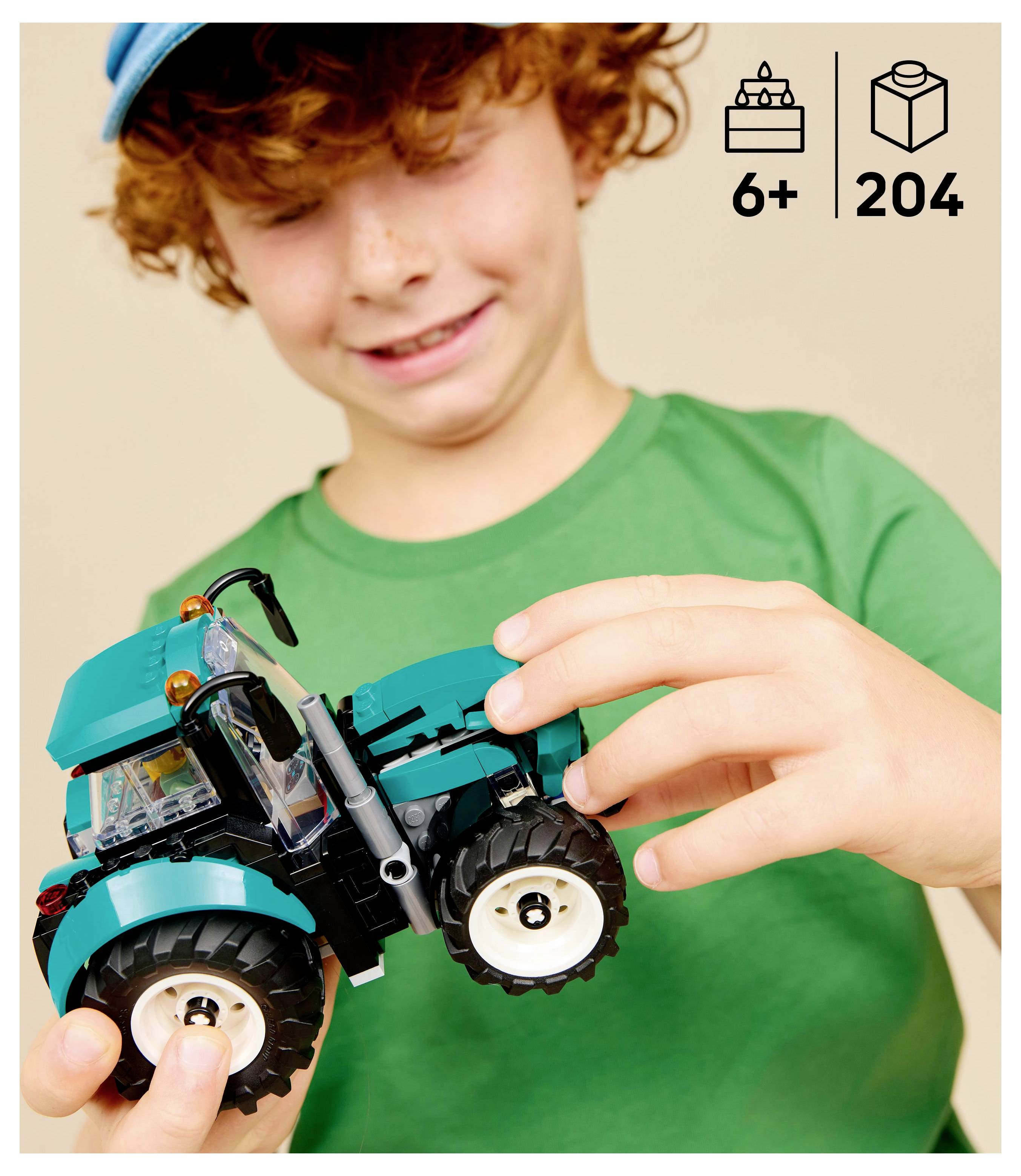 Ein Kind in einem grünen Shirt hält ein blaues Traktor-Spielzeug mit großen Rädern. Das Bild zeigt in der Ecke das Alter '6+' und die Teilezahl '204'.