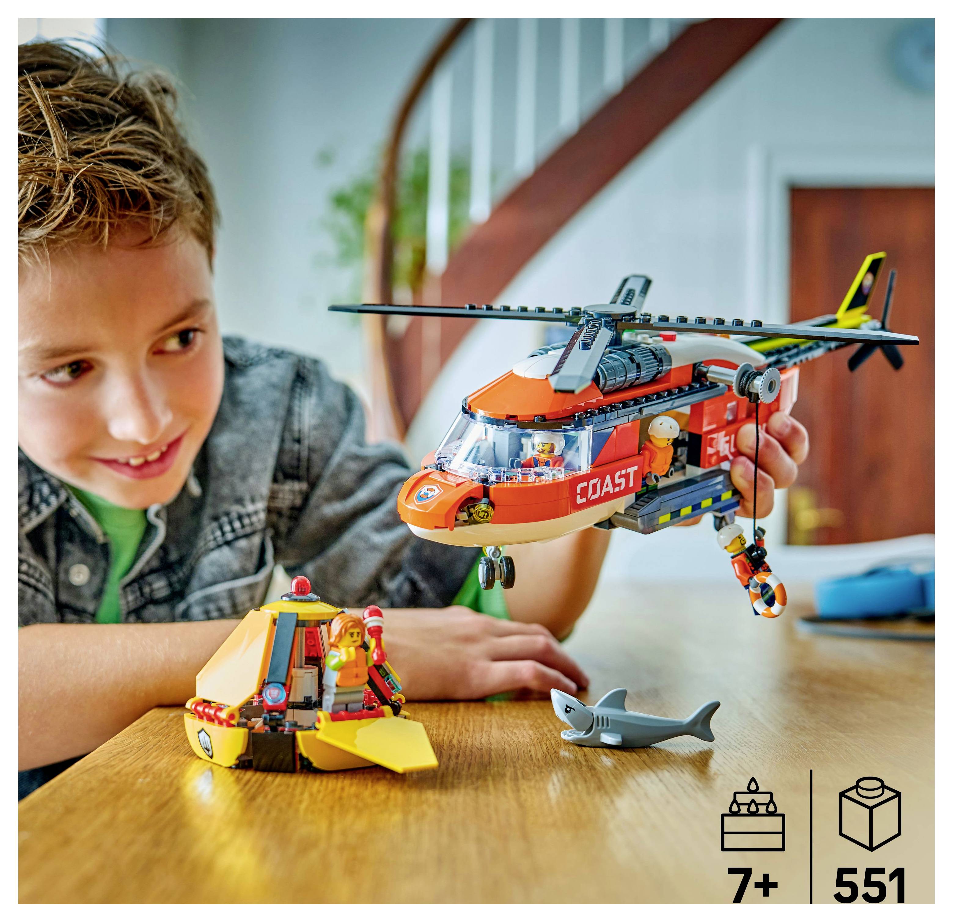 Kind spielt mit einem Spielzeug-Rettungshubschrauber und einem Boot auf einem Tisch. Das Set enthält einen kleinen Hai. Altersempfehlung ab 7 Jahren.